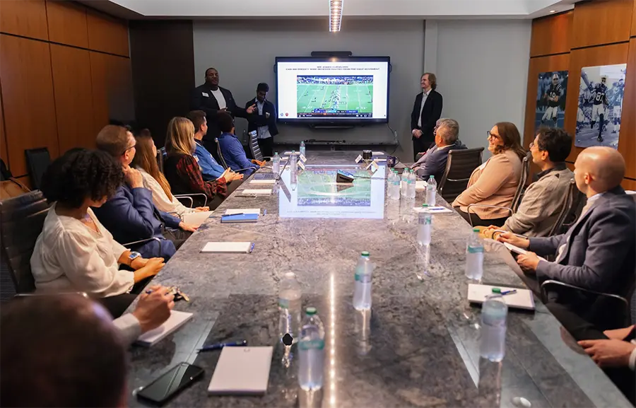 Board members seated at table looking at a presentation on a TV screen