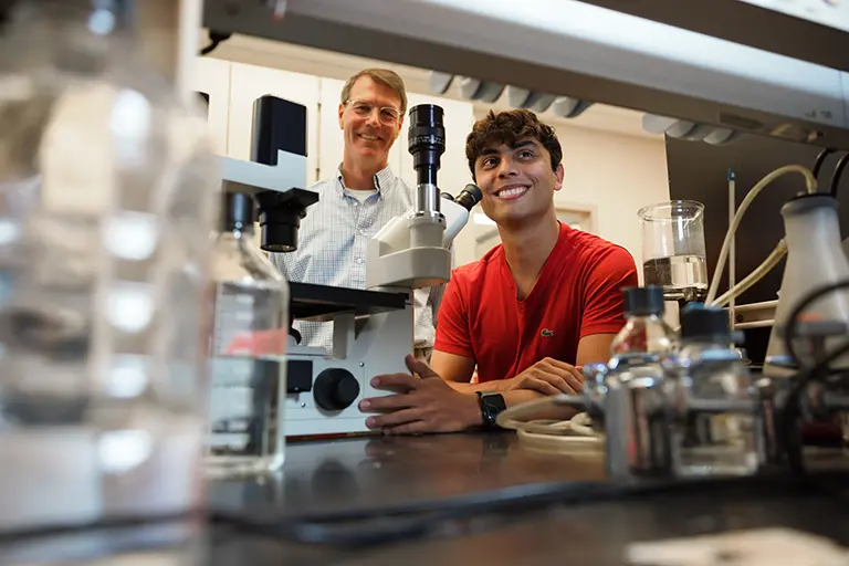 Student using a microscope in a lab and smiling