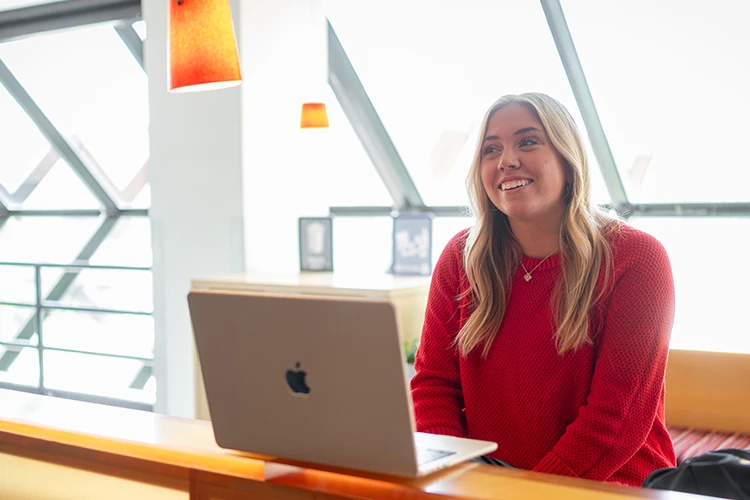 A student smiling in front of a laptop