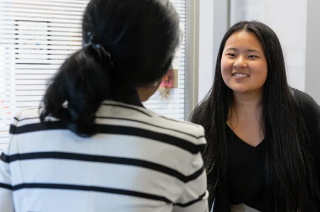 A student reaches out to shake the hand of a woman across from her.