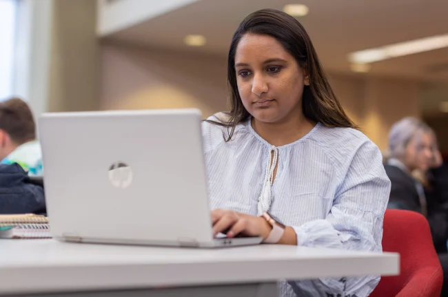 A student sits typing on her laptop at a table in University Library.